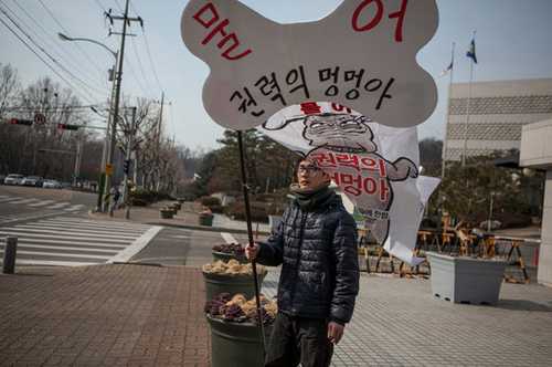 Park Sung-su, a political activist, protesting in front of the Supreme Court in Seoul, South Korea, last month. The sign, in Korean, reads, “Bite it off, you dogs of power.” Mr. Park was freed in December after being jailed on charges of defaming the president. JEAN CHUNG FOR THE NEW YORK TIMES지난달 한국 대법원 앞에서 시위하고 있는 정치 활동가 박성수 씨. 그가 든 팻말에는, 한국말로 “물어, 권력의 멍멍아”라고 쓰여있다. 박 씨는 대통령 명예훼손죄로 징역을 산 후 지난 12월에 풀려났다.
