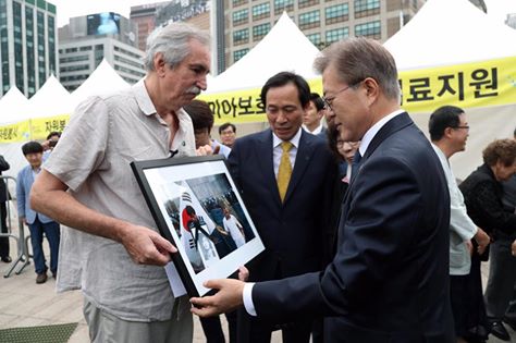 ▲ ‘MBC 6.10항쟁 다큐’의 주인공인 킴 뉴튼 교수가 지난 10일 서울광장에서 열린 6.10항쟁 30주년 기념식에서 문재인 대통령을 만나 6월항쟁 당시 찍은 사진과 함께 편지를 직접 전달하고 있다. <사진출처=문재인 대통령 페이스북>