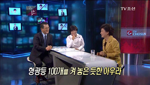 ▲ 2011년 12월 1일 TV조선 개국 당일 ‘시사토크 판’은 박근혜 전 한나라당 대표와의 인터뷰를 진행했다. ‘형광등 100개를 켜 놓은 듯한 아우라’ 등 노골적 미화 자막이 화제가 됐다. 왼쪽부터 당시 최희준 TV조선 앵커, 박은주 문화부장, 박근혜 전 대표. <이미지 출처=TV조선 화면 캡처>
